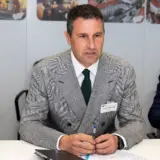Barna Tanczos, fostul ministru, este asezat la o masa intr-un cadru oficial, purtand un sacou in carouri si o cravata verde