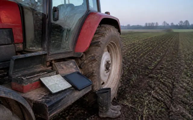 O imagine de aproape cu partea laterală a unui tractor roșu parcat pe un câmp arat