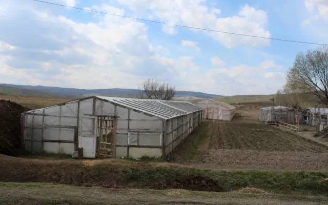 Two greenhouses on a small farm with a cultivated field and people walking in the distance