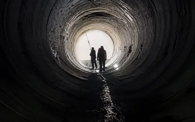 Silhouettes of two workers inside a massive water pipe at a construction site for irrigation infrastructure